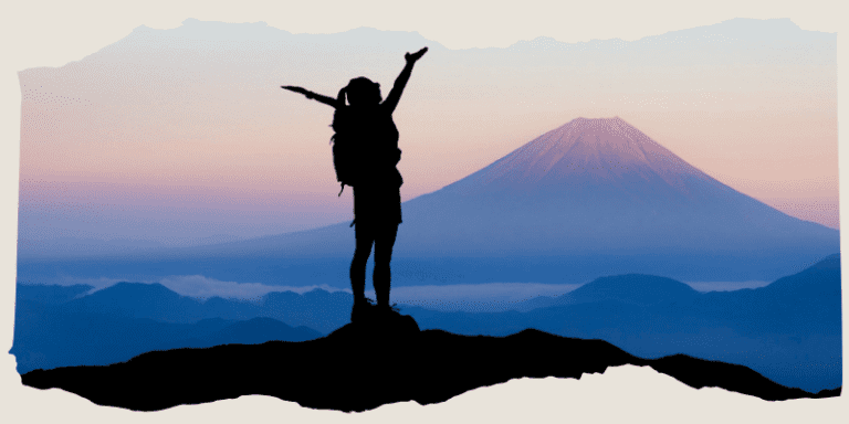 Frau steht auf einem Berg und streckt die Arme in die Höhe. Sie schaut auf einen Vulkan, den man im Hintergrund erkennen kann