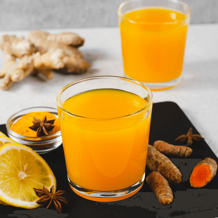 zwei Gläser mit einem orangenen Getränk, daneben Kurkuma Knollen und Orangenscheiben