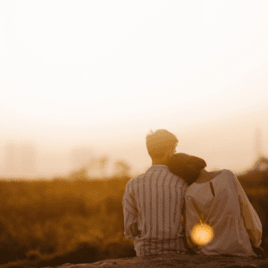 Paar sitzt aneinander gelehnt draußen und schaut in den Sonnenuntergang