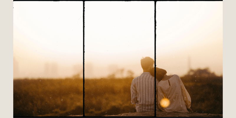 Du siehst ein Paar von hinten, welches sich aneinander lehnt und in den Sonnenuntergang blickt