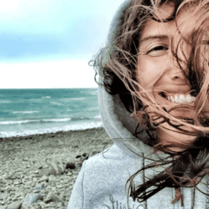 Frau lacht, Haare wehen, Meer im Hintergrund