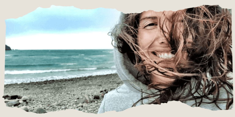 Frau lacht, Haare wehen im Wind, im Hintergrund ist das Meer