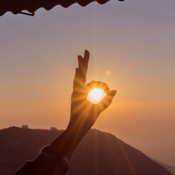 eine Hand formt mit dem Daumen und Zeigefinger einen Kreis und umrahmt damit die Sonne